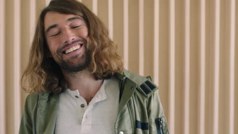 Primer-Plano-Retrato-De-Un-Joven-Caucásico-Relajado-Y-Amigable-Con-El-Pelo-Largo-Riendo-Feliz-Mirando-La-Cámara-Alegre-Fondo-De-Madera-Masculino