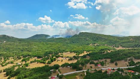 aerial tracking shot over a countryside town with wildfire background, sunny day