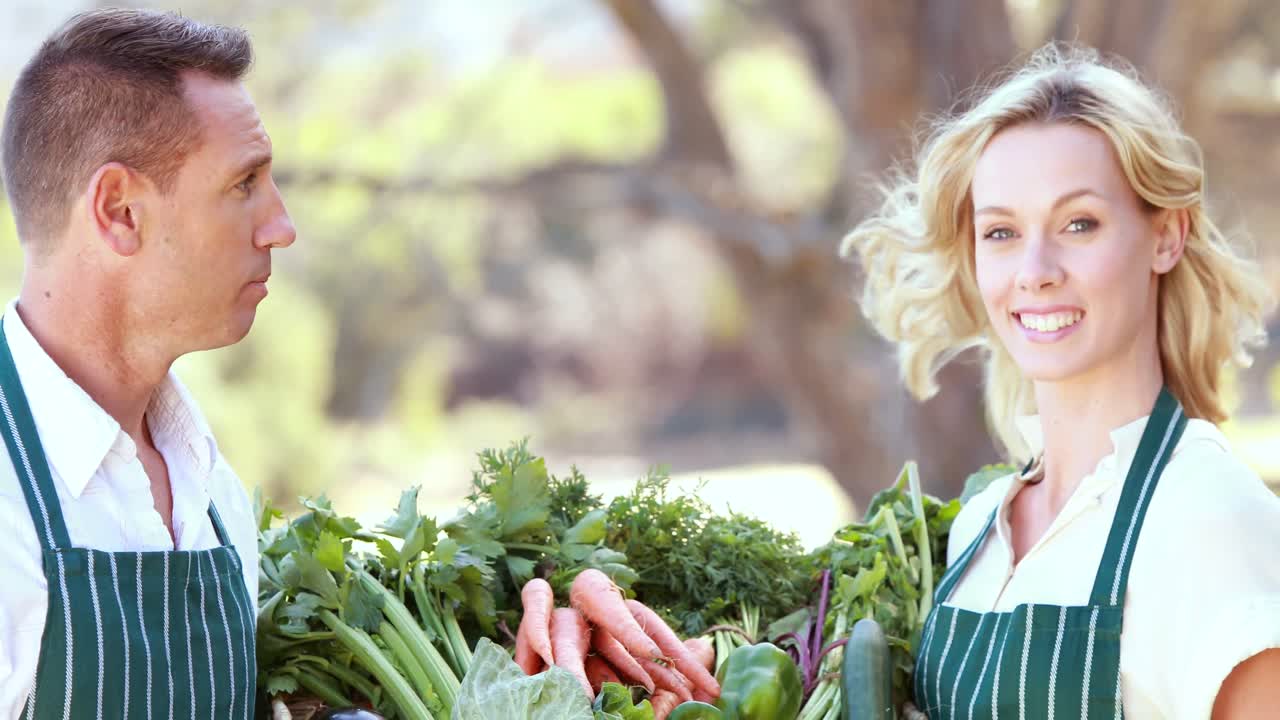 pareja de granjeros sonrientes sosteniendo una canasta de verduras
