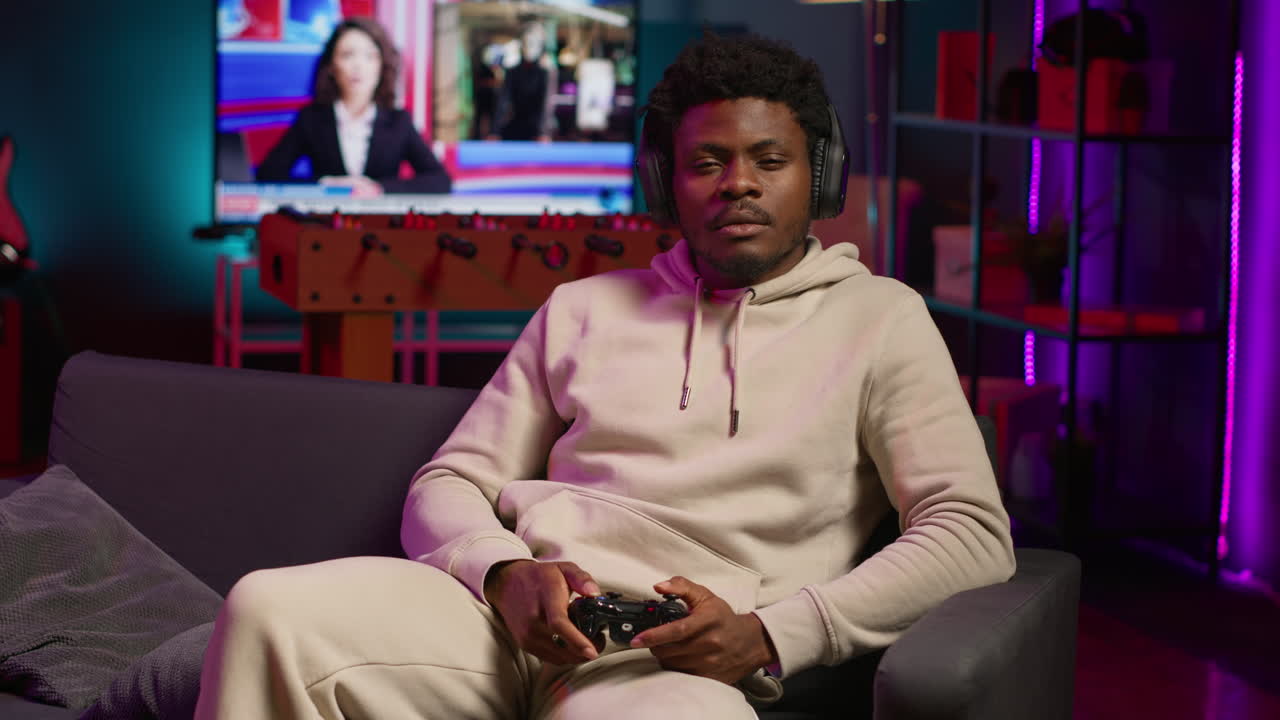 Bored guy plays online video game and spamming attack buttons on his controller, modern loft apartment. Gamer in neon lit space participating in internet e sports competition. Camera A.