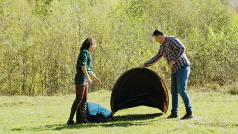 attractive young man and his girlfriend setting up tent for camping