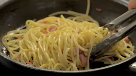 stirring hot pan with spaghetti pasta and chopped ham bacon