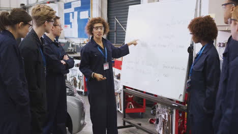 female tutor by whiteboard with students teaching auto mechanic apprenticeship at college