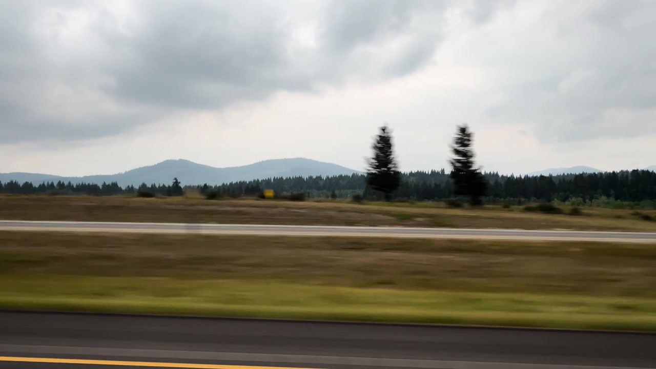 Vehicles drive along highway with forest and mountains under cloudy Alberta sky
