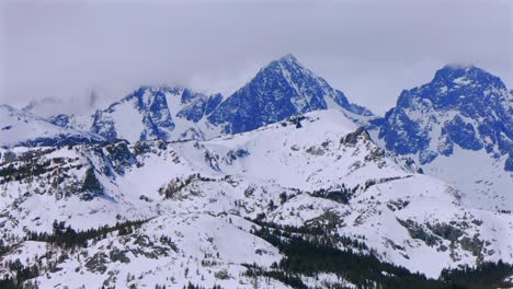 banner peak minaret summit pass mammoth mountains vista parallax winter aerial drone california group jagged towering snow covered peaks wind fog cloudy daytime alpine sierra nevada valley pan left