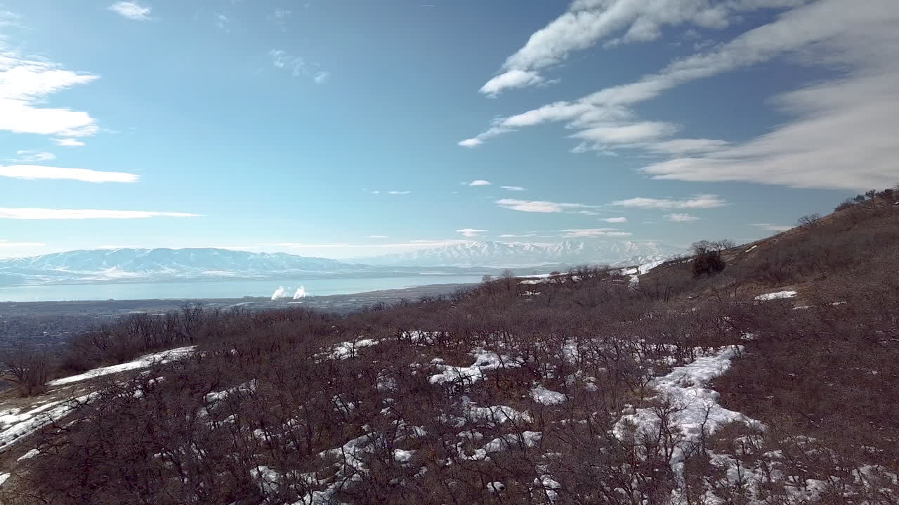 넓은 계곡에서 도시와 호수가 보이는 산기슭 위를 날다