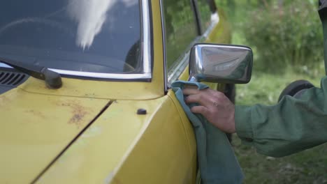 un hombre limpia un espejo lateral de un coche vintage amarillo pulido