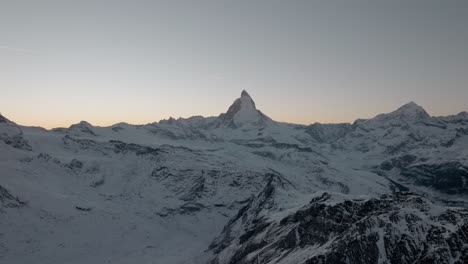 Mountain-drone-aerial-with-stunning-view-of-Matterhorn-Zermatt-in-Swiss-Alps-at-Sunset-during-winter-with-golden-clear-sky-and-airplane-flying-over