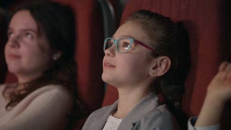 beautiful girl in glasses watching cartoon film in cinema. kid watching movie