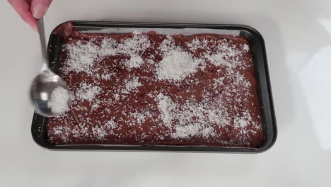 spreading coconut shavings on a caramel and chocolate slice