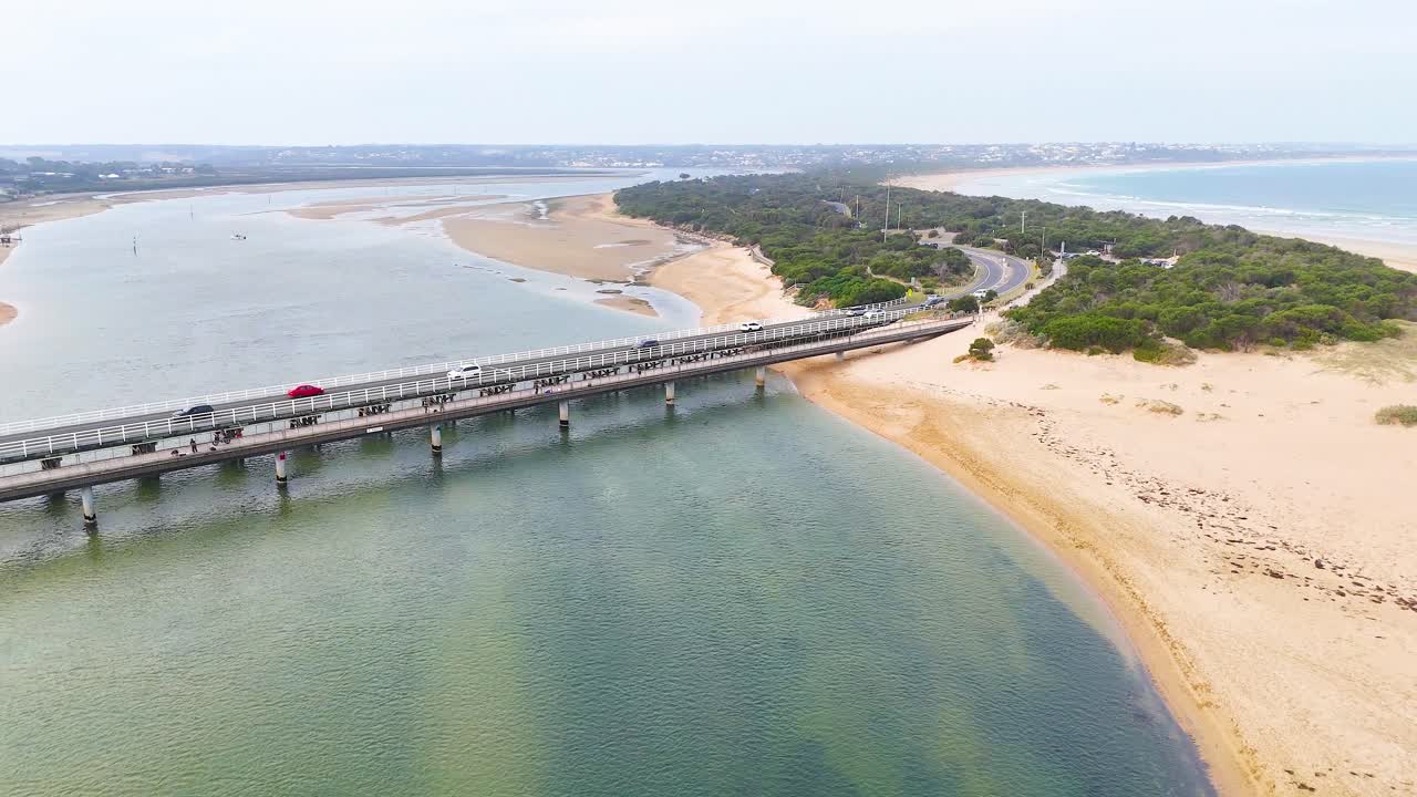 Aerial footage captures a vehicle crossing the Barwon Heads bridge over a serene river under soft daylight
