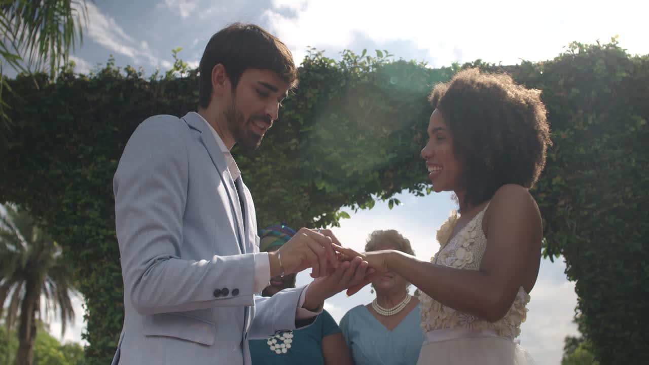 A happy couple exchanging rings and holding hands during their outdoor wedding ceremony
