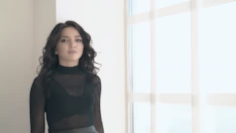 curly-haired-brunet-girl-stands-near-window-at-sunlight