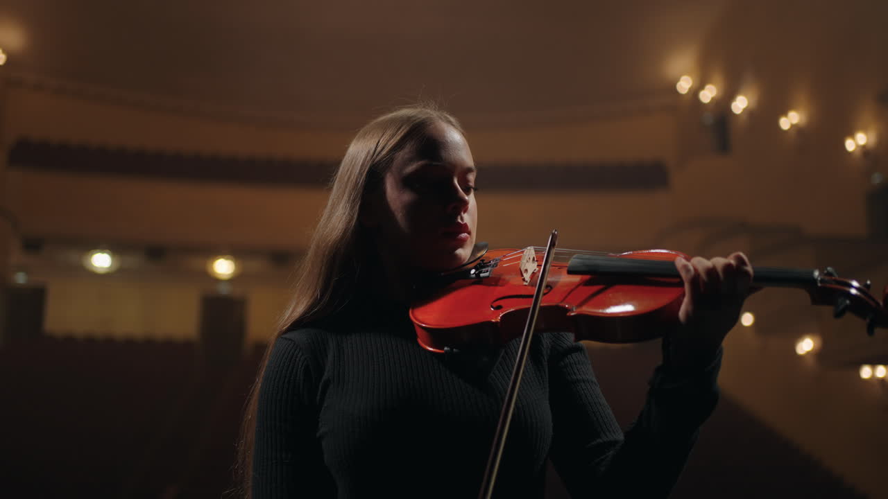 una mujer hermosa está tocando el violín rojo en una orquesta sinfónica en una ópera, un concierto de música clásica.