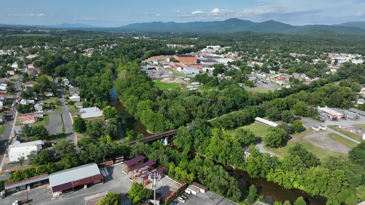 Aerial flyover American city with red brick buildings, river and industrial district in suburb. Sunny summer day in Waynesboro, Virginia. Blue ridge mountains on sunny day in distance. Wide shot