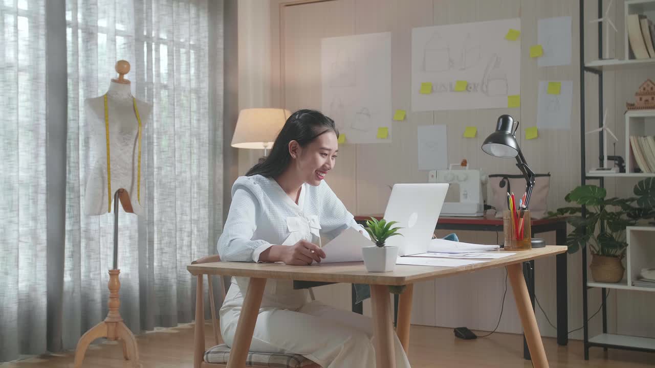 아시아 여성 디자이너가 사무실에서 노트북으로 작업하는 동안 레이아웃을 보고 있습니다.