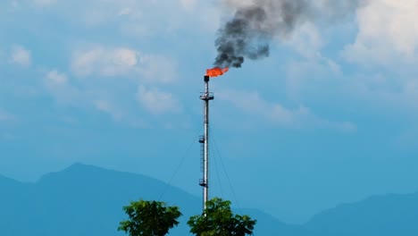 a flare stack burning off excess gas at an oil refinery with copy space in the hill background