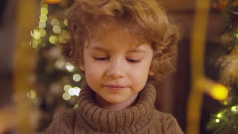 niño feliz con ojos verdes y cuello alto en primer plano, mira a la cámara mientras sostiene un regalo en navidad