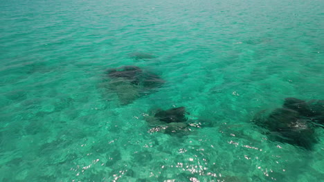 Vista-Sobre-El-Mar-De-Agua-Transparente-Con-La-Costa-En-El-Fondo-Durante-El-Verano-En-Cerdeña,-Italia---Toma-Aérea-De-Drones