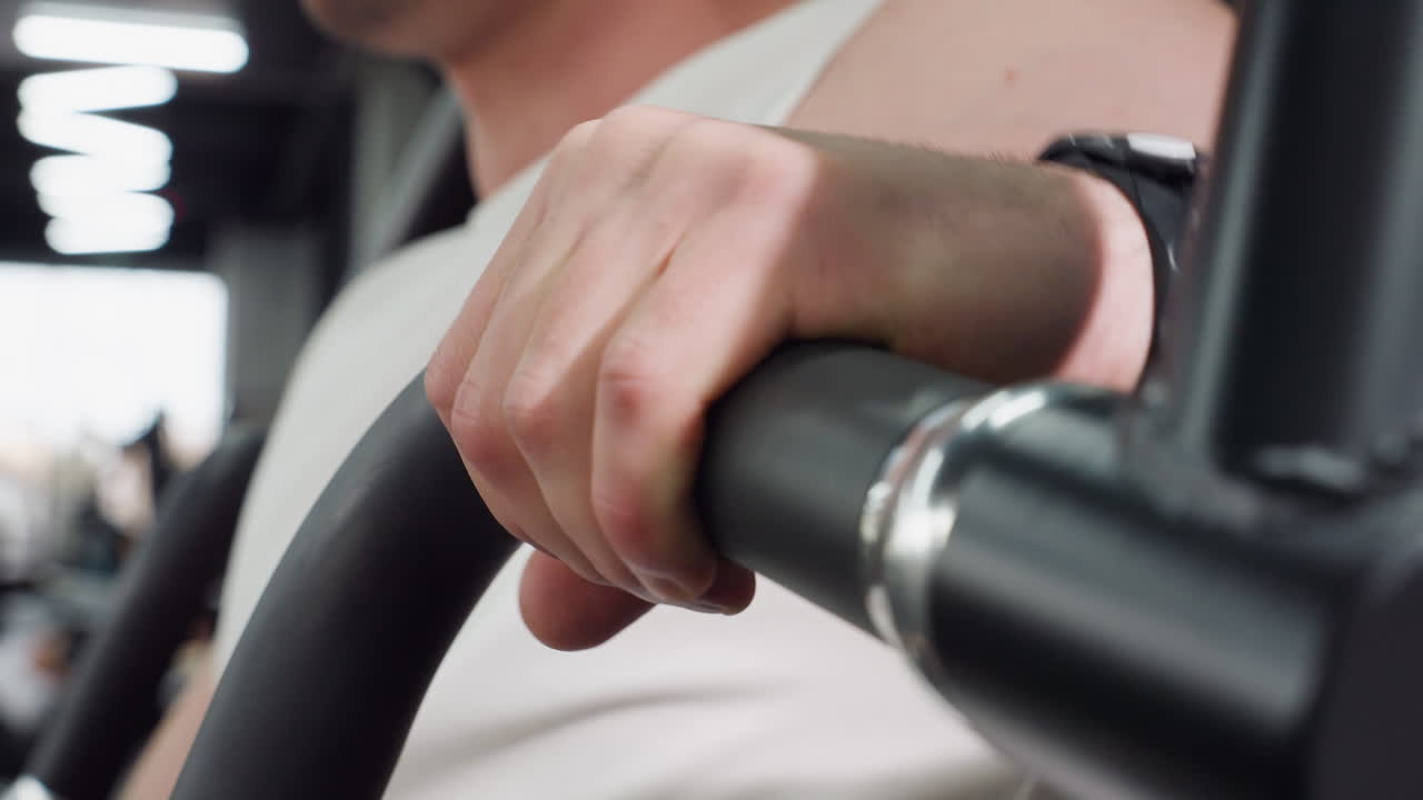 Close up view of student hand rolling over padded handle on weight machine in fitness room, fingers flexing under bright gym lights, focus captured as he prepares for strength training