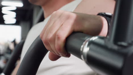 close up view of student hand rolling over padded handle on weight machine in fitness room, fingers flexing under bright gym lights, focus captured as he prepares for strength training