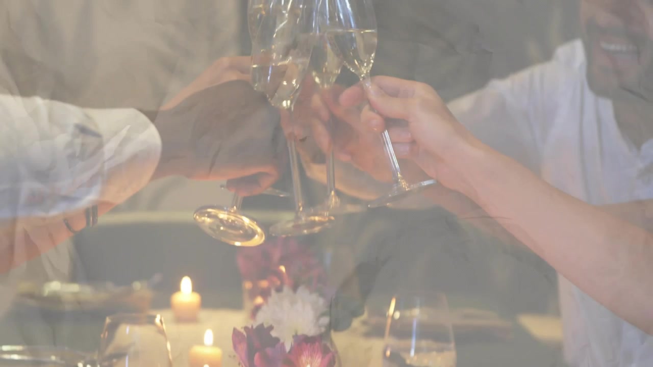 Vertical video: Smiling man in white shirt raising wine glass, friends toasting at candlelit table