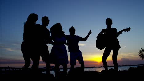 silhouette of friends dancing on beach at sunset