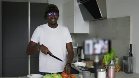 hombre africano de pie en la cocina registros en el teléfono celular nuevo blog de video de comida