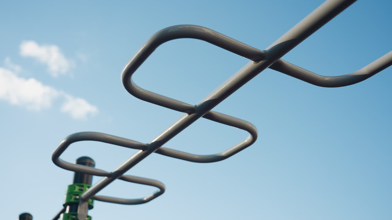 Sky view of silver colored outdoor pull up workout bars set against clear blue sky, modern park fitness station featuring monkey bar design, highlighting durable steel frame under bright daylight