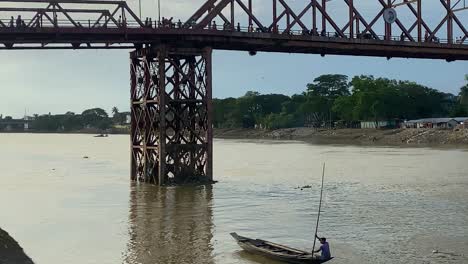 stunning shot of man kayaking in calm river under high suspended bridge, bangladesh