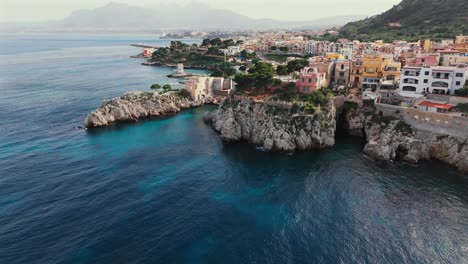 vibrant coastal scene in porticello, sicily showing colorful buildings, rocky cliffs, turquoise water and dramatic mediterranean seascape near palermo and bagheria