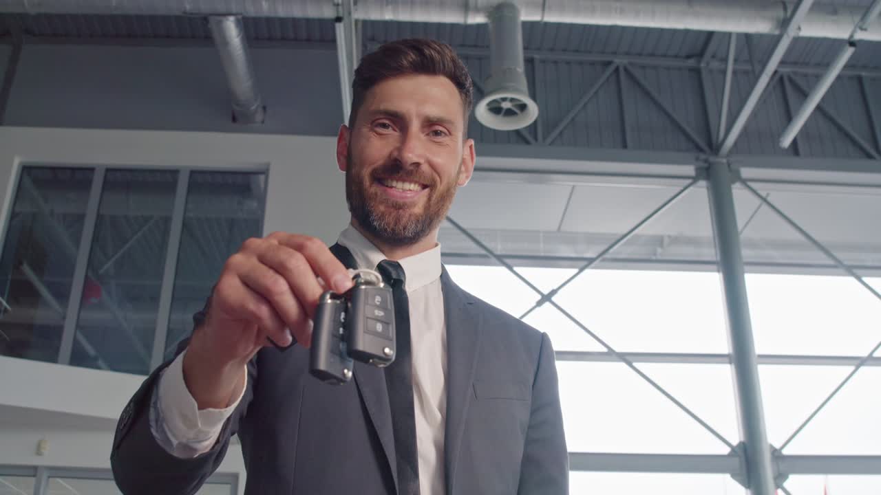 hombre de traje elegante sosteniendo las llaves de un auto nuevo en el salón