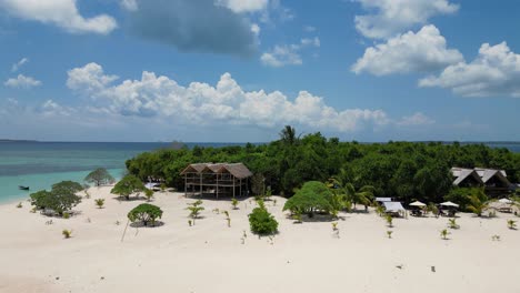 aerial pullback along white sandy beach and bungalow over banca boat and clear water