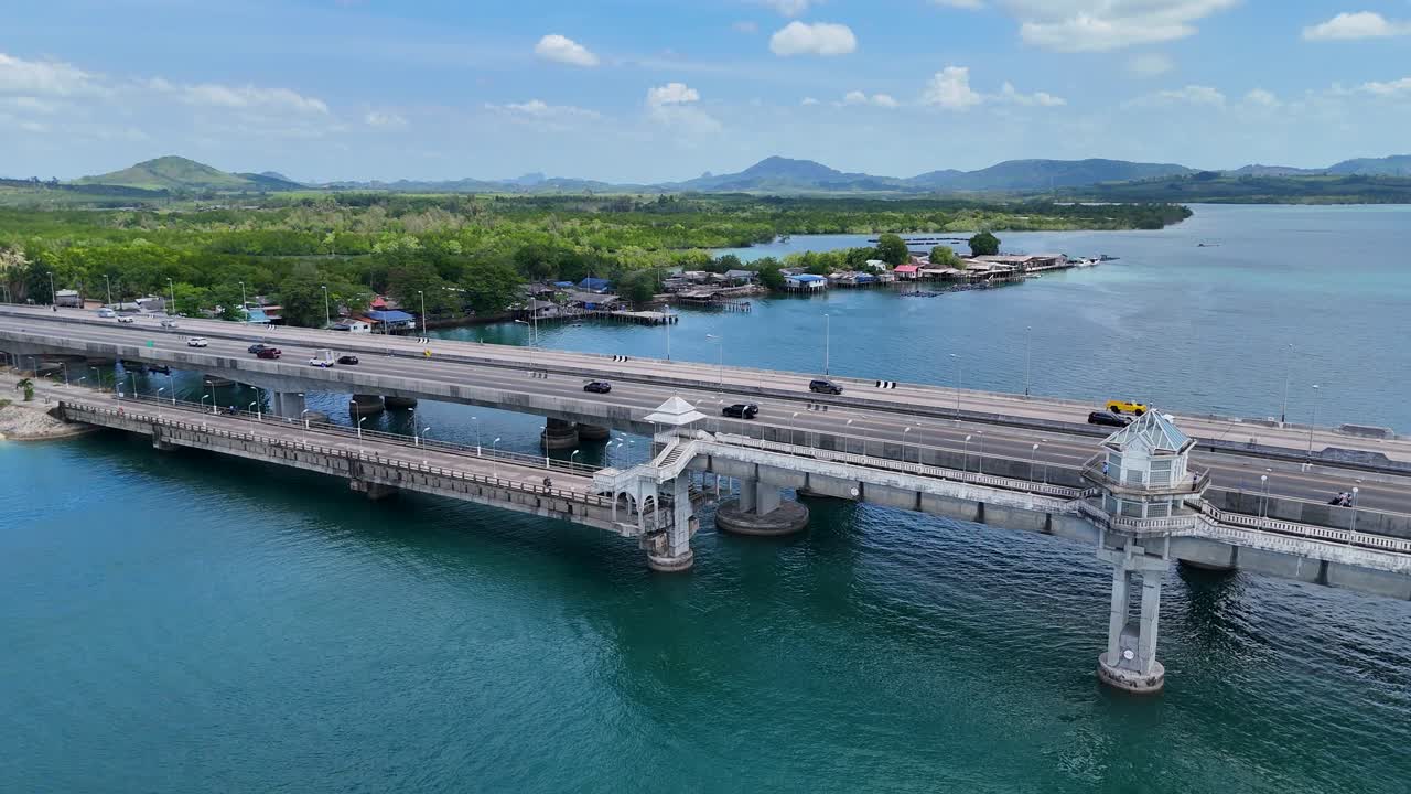 Drone footage captures Sarasin Bridge in Phuket, Thailand, with clear skies and turquoise waters, highlighting the bridge's architecture and surrounding landscape