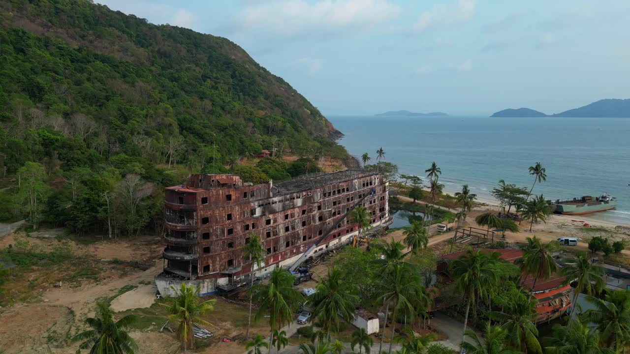 abandoned rusty ghost ship on Koh Chang on tropics island bay, Thailand, during sunset, with a crane working on it. Wonderful aerial view flight drone shot footage from above