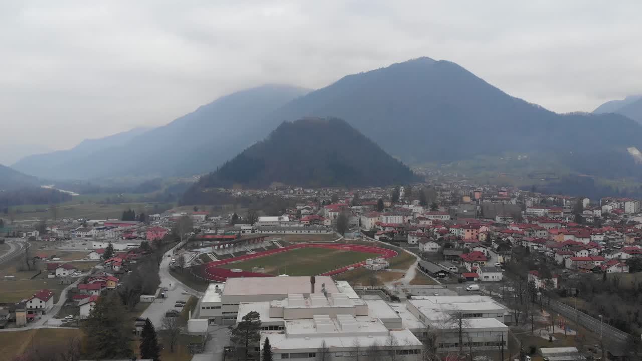 Aerial circular view of Tolmin on dull winter day, with a stadium and school in foreground