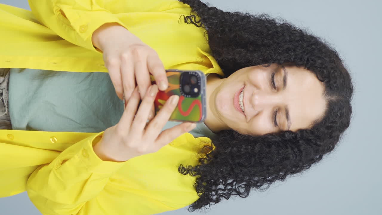 video vertical de una joven feliz enviando mensajes de texto por teléfono. sonriendo.