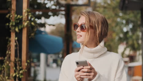 Kaukasische-Frau-Mit-Sonnenbrille-Und-Smartphone-Beim-Gehen-Im-Freien.