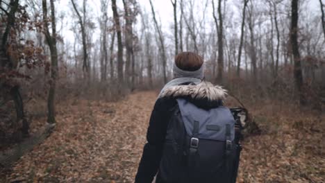 following shot of female caucasian photographer with backpack and tripod walking on leaf covered dirt road in forest