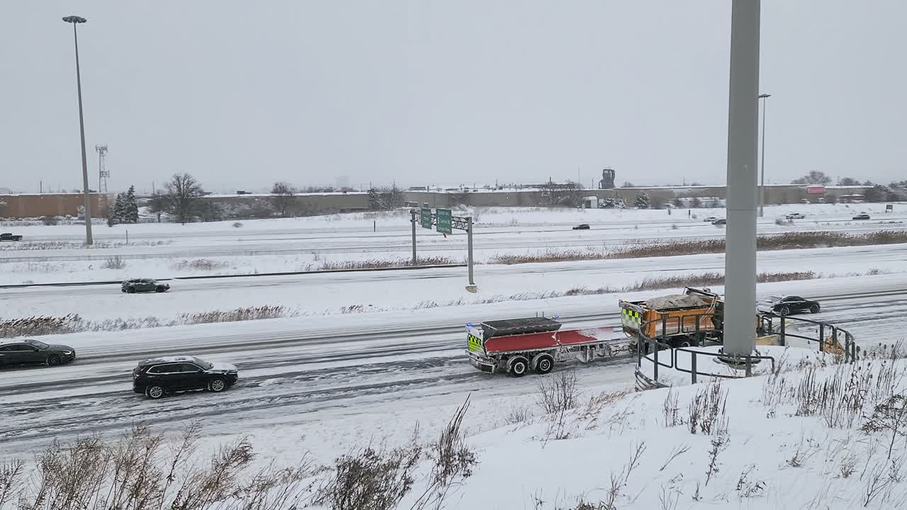 Snow plow truck clearing snowy highway after winter storm with heavy snowfall (Ontario, Canada). Yellow vehicle pushes snow while cars navigate icy road conditions in overcast weather