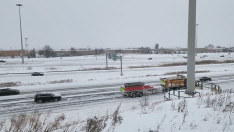 snow plow truck clearing snowy highway after winter storm with heavy snowfall (ontario, canada). yellow vehicle pushes snow while cars navigate icy road conditions in overcast weather