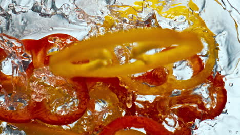 pimienta fresca cae líquido en súper cámara lenta. rojo amarillo sabroso pimentón de primer plano.