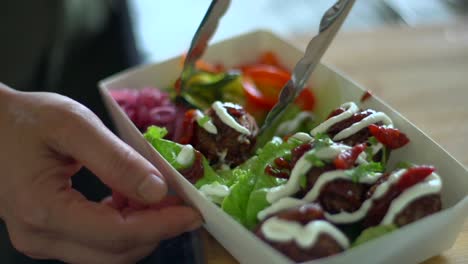 Meat-balls-being-rotated-and-positioned-in-container-of-salad,-filmed-as-close-up-shot-in-handheld-slow-motion-style