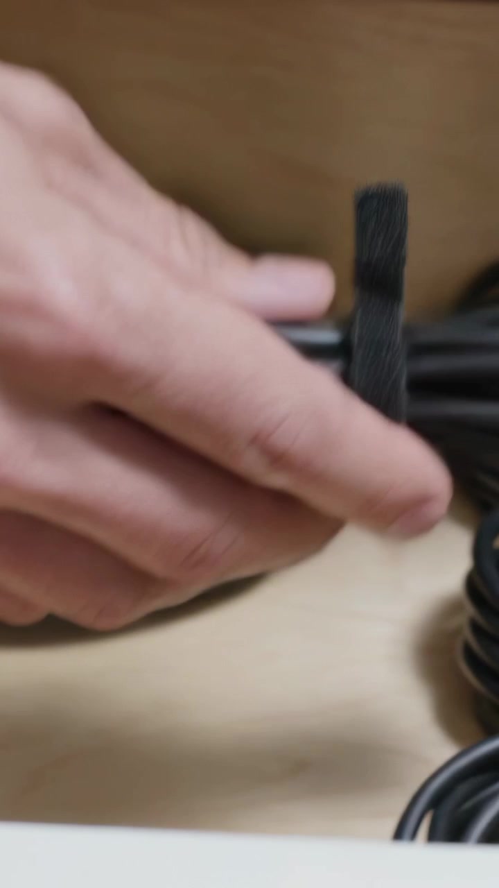 Vertical video: Hovering right hand lifting loose black cable on wood shelf, fastening velcro strap