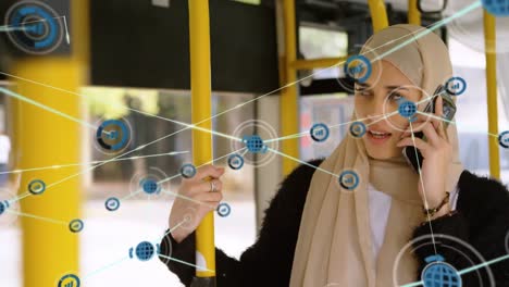 Animation-of-connected-icons-over-biracial-woman-wearing-hijab-talking-on-cellphone-in-bus