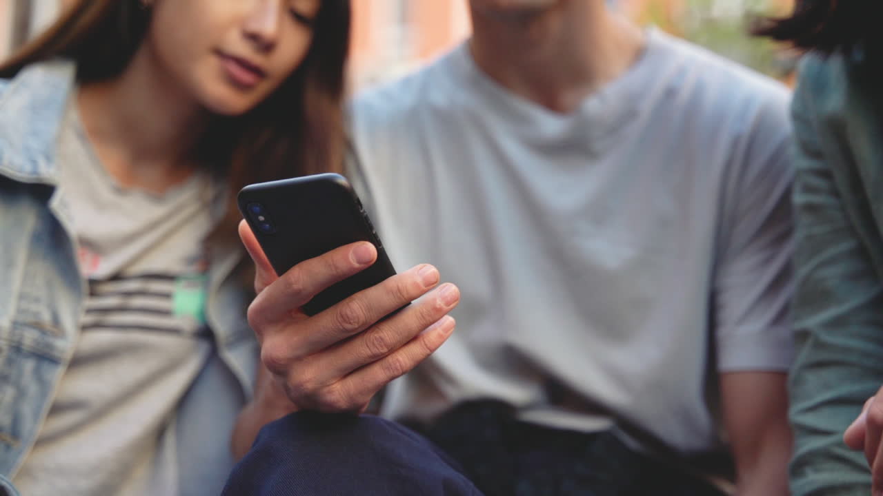 cerca de tres jóvenes amigos japoneses que buscan algo divertido en el teléfono móvil y se ríen mientras se sientan juntos en el parque