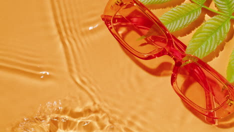 orange sunglasses on rippled water with leaves