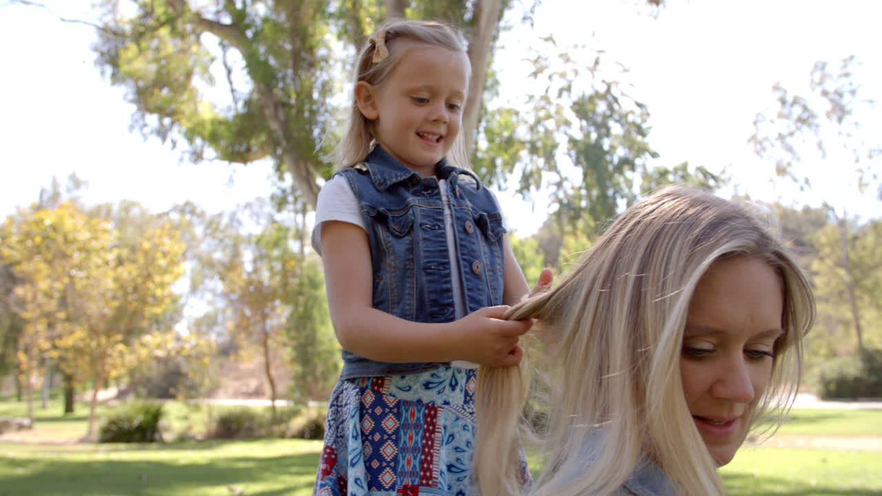 Young daughter braiding mother's hair in a park, front view