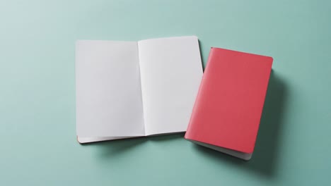 Close-up-of-open-blank-book-and-closed-red-book-with-copy-space-on-green-background-in-slow-motion