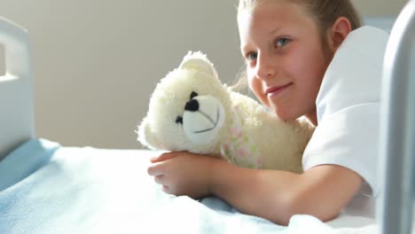 sick girl lying with teddy bear on bed